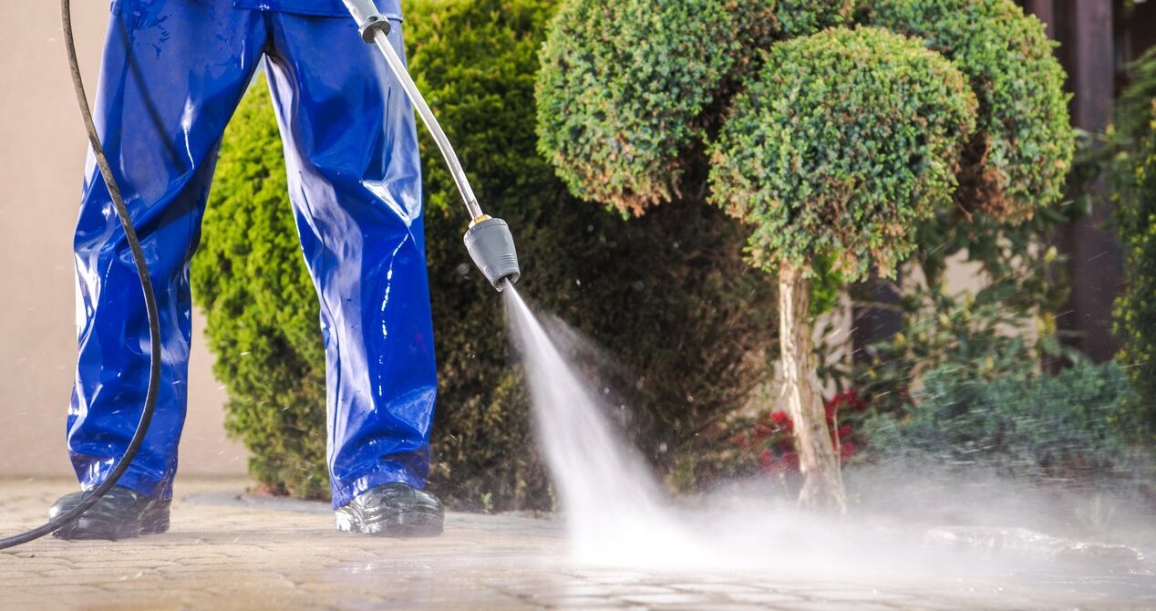 Pressure washing a stone patio next to garden shrubs